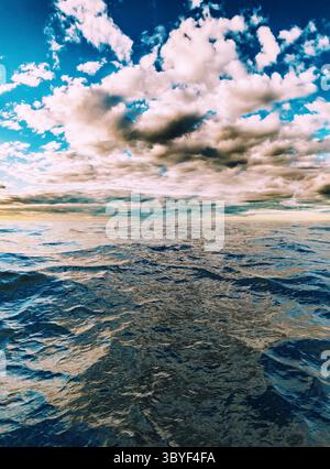 A bold cloud formation reflecting softly on rippling cool blue water in the foreground Stock Photo