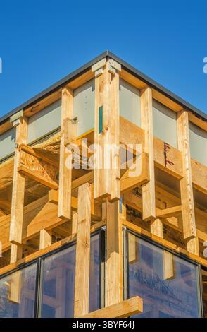 A wooden-framed building under construction, featuring large windows, set against a bright blue sky Stock Photo