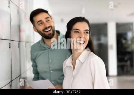 Two joyful colleagues laughing standing in modern coworking office Stock Photo