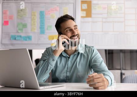 Smiling man lead talk on smartphone seated in workplace desk Stock Photo