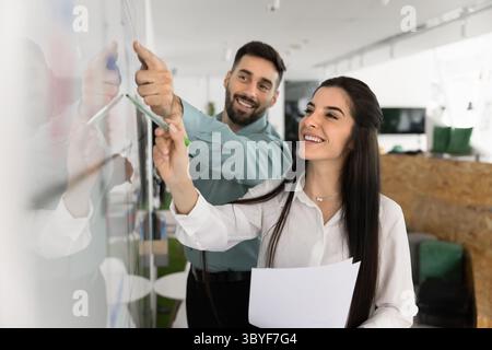 Two happy Latin workmates working together standing next to whiteboard Stock Photo