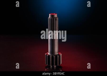 A dark gray, cylindrical component with a textured, gear-like end sits on a red surface. A blue and red gradient light illuminates the object Stock Photo