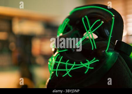 Neon-green hacker mask rests center stage on a cyber desk, while three widescreen monitors overflow with rapidly scrolling code. Stock Photo