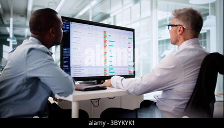 Focused Business Team Analyzing Reports On Multiple Computer Screens Together. Stock Photo