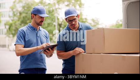 Hispanic Mover Unloading Boxes From Delivery Truck In Professional Uniform. Stock Photo
