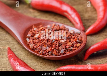Wooden spoon of dried chili pepper flakes among fresh peppers Stock Photo