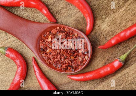 Wooden spoon of dried chili pepper flakes among fresh peppers Stock Photo