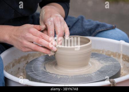 Close up of female potters hands making bowl. Woman cupped hands around wet clay on a potters wheel. Woman making ceramics in pottery workshop. Stock Photo