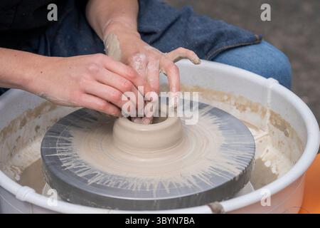 Close up of female potters hands making bowl. Woman cupped hands around wet clay on a potters wheel. Woman making ceramics in pottery workshop. Stock Photo
