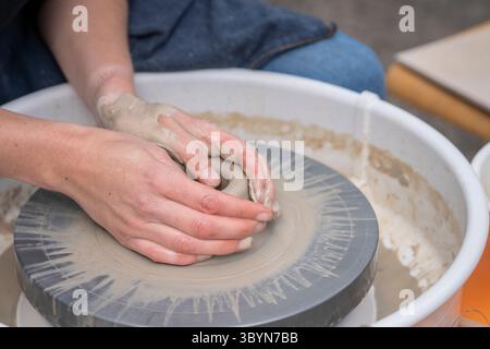 Close up of female potters hands making bowl. Woman cupped hands around wet clay on a potters wheel. Woman making ceramics in pottery workshop. Stock Photo