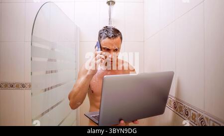 Busy man holding laptop and talking on phone while showering Stock Photo