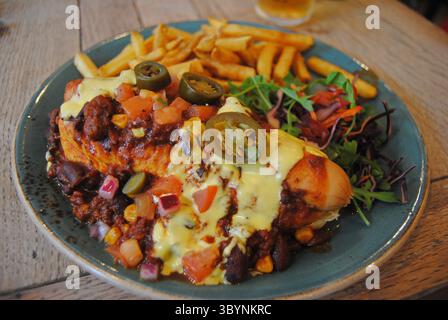 Loaded chili cheese dog with jalapenos, French fries, and side salad on rustic table Stock Photo