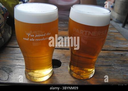 Leeds, Great Britain – June 22, 2014. Two pints of craft beer on rustic table – real ale with frothy head in authentic pub setting. Stock Photo