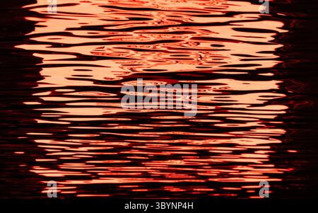 The image is of a body of water with red waves. The water appears to be calm and peaceful, with the waves gently lapping against the shore. The red co Stock Photo