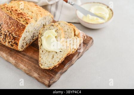 Tasty multigrain french bread with butter on cutting board with knife on light table, closeup. Space for text. Stock Photo