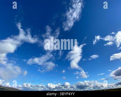 The vibrant blue sky is filled with puffy white clouds on a beautiful day. Stock Photo