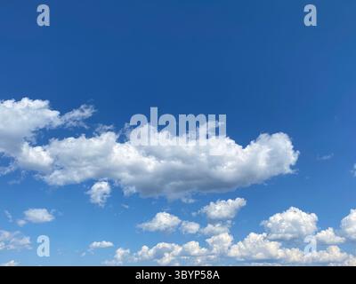 The vibrant blue sky is filled with puffy white clouds on a beautiful day. Stock Photo