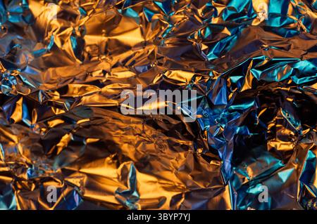 A close-up shot of crumpled aluminum foil, illuminated with a vibrant mix of orange and blue light, creating a dynamic and abstract texture. Stock Photo