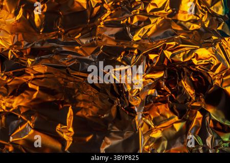 A close-up shot of crumpled aluminum foil, illuminated with warm, golden light, creating a textured and abstract pattern. Stock Photo