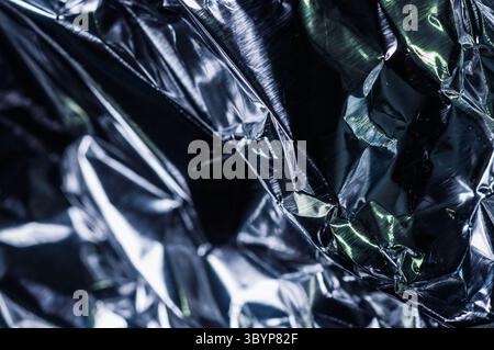 A close-up shot reveals the intricate folds and reflective surface of crumpled silver foil, capturing the play of light and shadow across its metallic Stock Photo