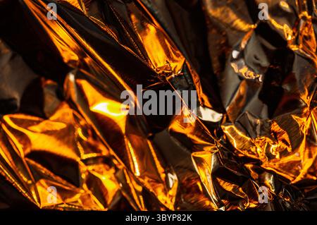 A close-up shot reveals the intricate folds and shimmering surface of crumpled gold foil, reflecting light and shadow in a dynamic display of texture Stock Photo