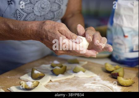 Preparation of homemade fruit dumplings with plums. Czech specialty of sweet good food. Dough on kitchen wooden table with hands Stock Photo