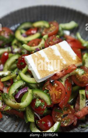 Salad made with fresh tomatoes, cucumbers, red onions, parsley, and dill topped with a thick slice of grilled halloumi cheese Stock Photo