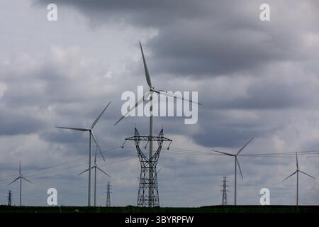 Aerial panorama of cascading wind turbines and power pylons under dramatic clouds over Amsterdam’s flat polder showcasing renewable energy convergence Stock Photo