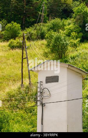 A utility structure stands in a rural area surrounded by lush green hills. Power lines run overhead, connecting the remote site to the electric grid o Stock Photo