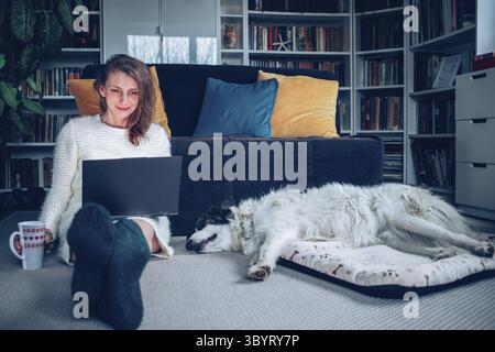 Woman using laptop at home with dog hygge Stock Photo