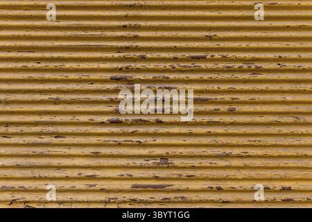 Rustic background on the street. Old garage door. Yellow painted, rusted corrugated metal sheet. Close up of wavy metal plate Stock Photo
