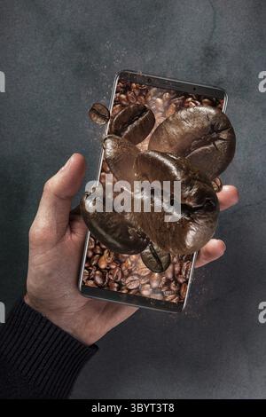 Mobile phone and fresh roasted falling coffee beans concept with concrete background. Man holding phon withflying coffee beans Stock Photo