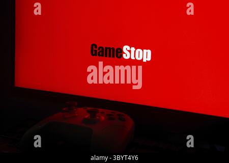 GameStop logo on a bright red screen with a gaming controller in the dark foreground Stock Photo