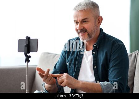 Cheerful matured man broadcasting from home, using smartphone Stock Photo