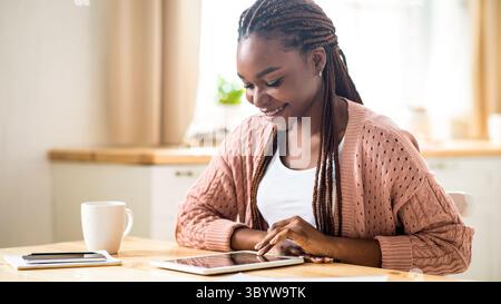 Happy Young Black Woman Using Digital Tablet In Kitchen At Home Stock Photo