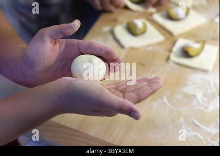 Preparation of homemade fruit dumplings with plums. Czech specialty of sweet good food. Dough on kitchen wooden table with hands Stock Photo
