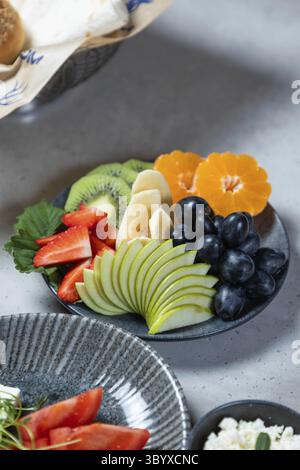 Plate of sliced fruits, including apples, bananas, grapes, and oranges, offers a refreshing and nutritious start to the day Stock Photo