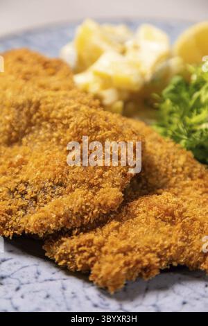 Breaded chicken schnitzel is served on a plate with potatoes salad and garnish Stock Photo