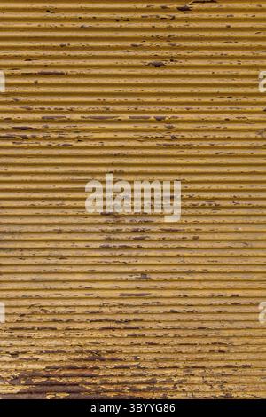 Rustic background on the street. Old garage door. Yellow painted, rusted corrugated metal sheet. Close up of wavy metal plate Stock Photo