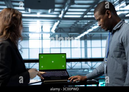Admins using green screen laptop in data center, managing server virtualization. IT professionals using chroma key notebook in server room, sustaining long term infrastructure reliability Stock Photo