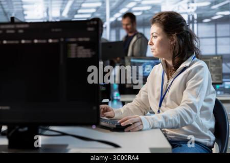 System administrator in data center coordinating deployment of server architecture, improving data processing speed. Woman in server farm configuring and testing hardware using PC Stock Photo