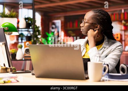 Remote worker pausing work done on laptop at home to pensive thinking. African american teleworker in apartment feeling bored by repetitive tasks, stopping work on notebook to daydream Stock Photo