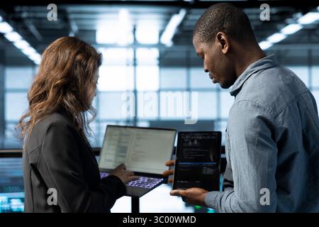 Software developers in data center automating routine maintenance tasks with laptop, executing diagnostic scripts. Server hub IT professionals coding on notebook, adjusting power settings Stock Photo
