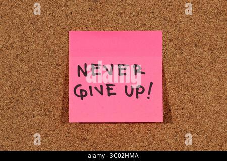 Close up to a sticky note with "never give up" positive motivational phrase over a cork background Stock Photo