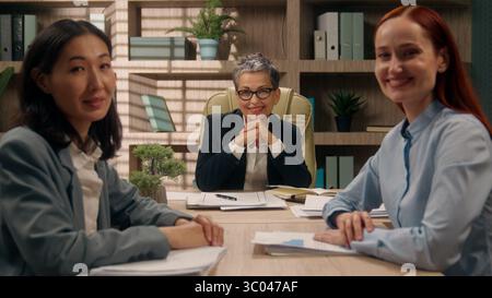 Three multiracial happy females business team businesswomen coworkers office girls group colleagues portrait Caucasian Asian women smiling posing Stock Photo