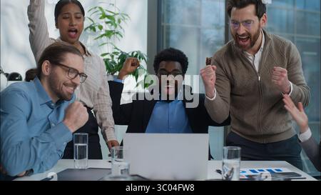 Excited happy multiethnic business workers in office Caucasian businesswomen African businessmen team colleagues multiracial group looking laptop Stock Photo