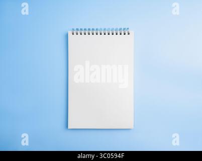 Blank vertical notepad isolated on horizontal blue background. Empty white paper, spiral notebook page template, mockup space for write, draw, short n Stock Photo
