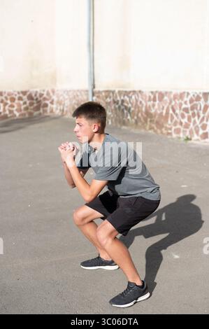 Teenager doing squats outdoors, focused and determined during his workout. Stock Photo