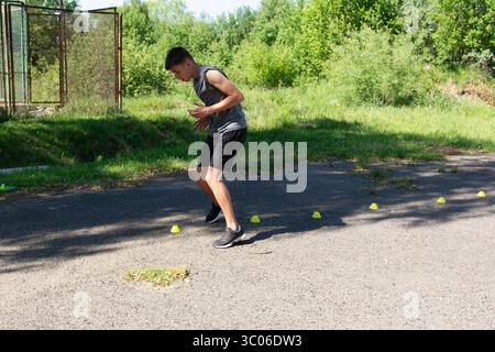 Young man doing agility training outdoors, navigating a course of cones. He's focused and athletic. Stock Photo