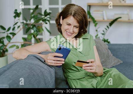 Caucasian Middle Aged Woman Shopping Online Using Smartphone and Credit Card Stock Photo